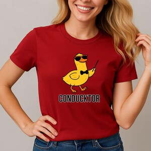 T-shirt featuring a cartoon duck wearing sunglasses and a bow tie, holding a conductor’s baton, with the word “CONDUCKTOR” printed below as a music pun.