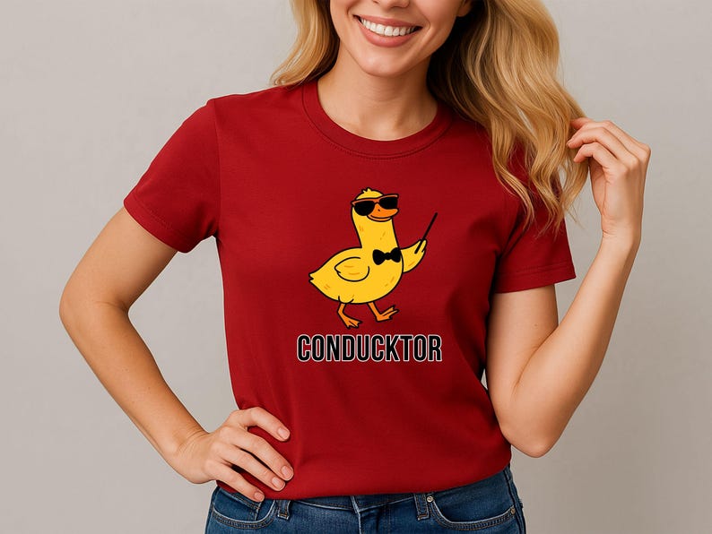 T-shirt featuring a cartoon duck wearing sunglasses and a bow tie, holding a conductor’s baton, with the word “CONDUCKTOR” printed below as a music pun.