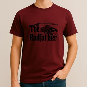 Puede incluir: Camiseta granate con un gr&aacute;fico negro. El gr&aacute;fico presenta un esqueleto de pez con una ca&ntilde;a de pescar y el texto "The Rodfather". La camiseta es de material suave y es adecuada para uso casual.