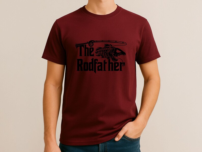Puede incluir: Camiseta granate con un gr&aacute;fico negro. El gr&aacute;fico presenta un esqueleto de pez con una ca&ntilde;a de pescar y el texto "The Rodfather". La camiseta es de material suave y es adecuada para uso casual.