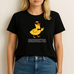 T-shirt featuring a cartoon duck wearing sunglasses and a bow tie, holding a conductor’s baton, with the word “CONDUCKTOR” printed below as a music pun.