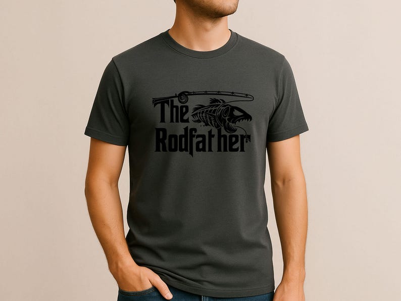 Puede incluir: Camiseta gris oscuro con un gr&aacute;fico negro de un esqueleto de pez y una ca&ntilde;a de pescar. El texto "The Rodfather" est&aacute; debajo en una fuente estilizada. La camiseta es de material suave.