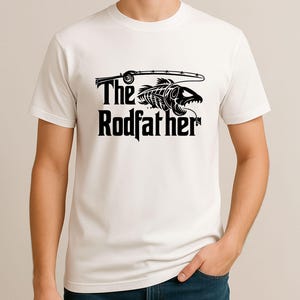 Puede incluir: Camiseta blanca con un dise&ntilde;o gr&aacute;fico negro. El dise&ntilde;o presenta una ca&ntilde;a de pescar, un esqueleto de pez y las palabras "The Rodfather" en negrita y con un estilo llamativo. La camiseta es de manga corta y parece ser de algod&oacute;n.