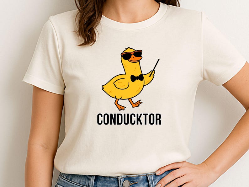 T-shirt featuring a cartoon duck wearing sunglasses and a bow tie, holding a conductor’s baton, with the word “CONDUCKTOR” printed below as a music pun.