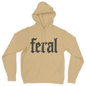 Op de afbeelding: Een beige hoodie met een voorzak en een capuchon. Het woord "feral" is in een gotisch lettertype in donkergrijs op de borst gedrukt.