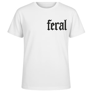 Op de afbeelding: Wit T-shirt met ronde hals en het woord "feral" in zwarte gotische letters op de linkerborst. Het shirt met korte mouwen heeft een klassieke pasvorm, geschikt voor dagelijks gebruik.