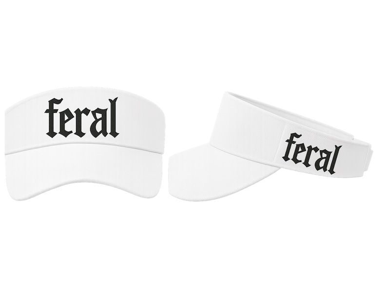 Op de afbeelding: Twee witte vizieren met het woord "feral" in zwarte gotische letters. De vizieren worden vanuit verschillende hoeken getoond, &eacute;&eacute;n recht van voren en de andere in een lichte hoek, waarbij het ontwerp wordt benadrukt.