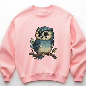 May include: A light pink sweatshirt featuring a cartoon owl perched on a branch. The owl has large eyes, blue and tan feathers, and is surrounded by green leaves. The sweatshirt is a solid color.