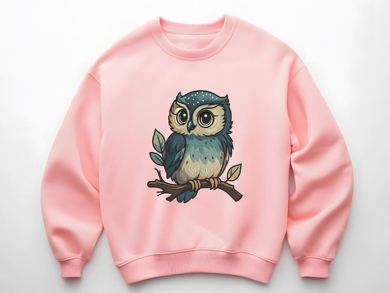 May include: A light pink sweatshirt featuring a cartoon owl perched on a branch. The owl has large eyes, blue and tan feathers, and is surrounded by green leaves. The sweatshirt is a solid color.