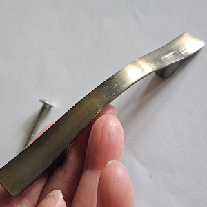 May include: A brushed nickel cabinet pull with a curved design. The pull has a satin finish and is approximately 4 inches long.