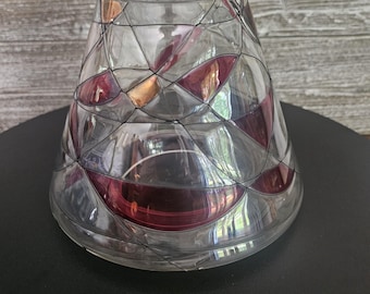 May include: A clear glass hurricane candle holder with a tapered, conical shape. The surface features a geometric pattern of dark red and metallic copper-colored triangular glass segments outlined in thin black lines, creating a stained-glass effect.