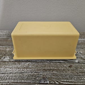 May include: A yellow plastic butter dish with a white base. The dish has a circular design on the top.