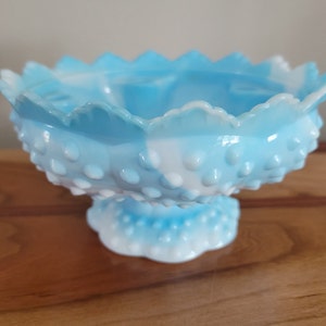 May include: A blue and white milk glass candy dish with a scalloped edge and a pedestal base. The dish is covered in small white dots.