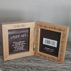 May include: A light-colored wooden double picture frame with the words "I Love You" engraved around the edges. The frame is open, revealing the text "LASER ART" and product details.