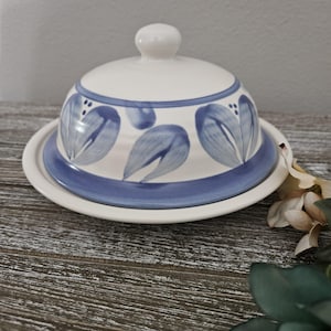 May include: A white ceramic butter dish with a blue and white floral design. The dish has a lid and a base.