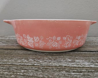 May include: A pink casserole dish with a white floral pattern. The dish has two handles and is made of ceramic.