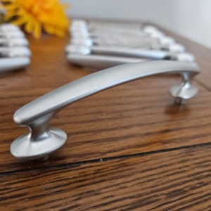 May include: A set of three ceramic mugs with a speckled, cream-colored glaze. Each mug features a different hand-painted design: a blue and green leaf, a yellow flower, and a red berry. The mugs have a simple, modern design.