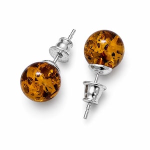 May include: A pair of stud earrings featuring round amber stones with a silver post and backing. The amber stones have a warm, golden-brown color with visible inclusions. The earrings are set against a white background.