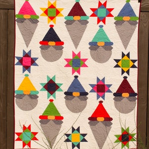 May include: A quilt featuring a patchwork design with gnomes and stars. The gnomes are wearing different colored hats and have white beards. The stars are in various colors and patterns.