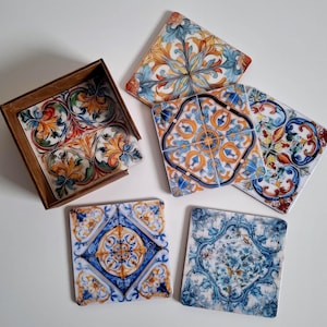 Può includere: Un set di sottobicchieri quadrati in ceramica con disegni ornati e colorati. I sottobicchieri presentano motivi nei toni del blu, arancione, giallo e verde. Sono esposti con un supporto in legno.