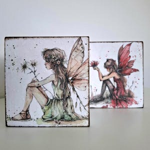 Puede incluir: Dos piezas de arte cuadradas con ilustraciones de hadas. Una muestra un hada con un vestido verde y grandes alas, la otra un hada con un vestido rojo. Ambas están sentadas y sostienen flores, sobre un fondo blanco.