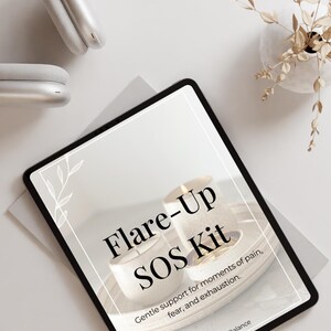 Op de afbeelding: Een digitale tablet met een afbeelding met de tekst "Flare-Up SOS Kit" en de bijschrift "Gentle support for moments of pain, fear, and exhaustion." De afbeelding heeft een witte achtergrond met een houten dienblad en twee kaarsen. De tablet ligt op een wit oppervlak met een koptelefoon en een kleine vaas met gedroogde bloemen.
