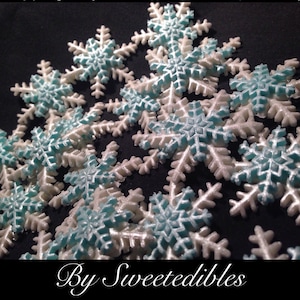 May include: A collection of white and light blue snowflake sprinkles. The snowflakes are made of sugar and are perfect for decorating cakes, cupcakes, and other desserts.