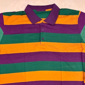 May include: A polo shirt with horizontal stripes in purple, green, and orange. The shirt has a purple collar and a three-button placket. The sleeves are green. The shirt is made of a soft, likely cotton, material.