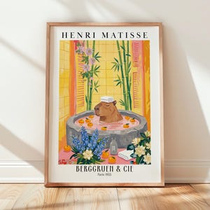 May include: A framed art print titled HENRI MATISSE BERGGRUEN & CIE Paris 1953 featuring a capybara with a white towel on its head soaking in a stone tub filled with pink water and oranges, surrounded by bamboo, blue flowers, and white blossoms.