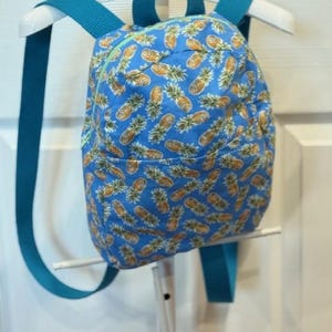 May include: A small blue backpack with a pineapple print and teal straps.