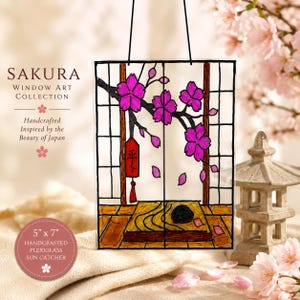 May include: A rectangular plexiglass sun catcher measuring 5 inches by 7 inches, featuring a black-lined illustration of a cherry blossom branch with bright pink flowers, a red hanging tag with black text, and a wooden floor interior scene.