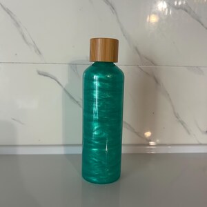 Peut inclure: Une bouteille turquoise avec un bouchon en bois. La bouteille a un aspect scintillant et pailleté. La bouteille cylindrique est probablement en verre ou dans un matériau similaire. Le bouchon en bois offre un contraste naturel. La bouteille mesure environ 15 cm de haut.