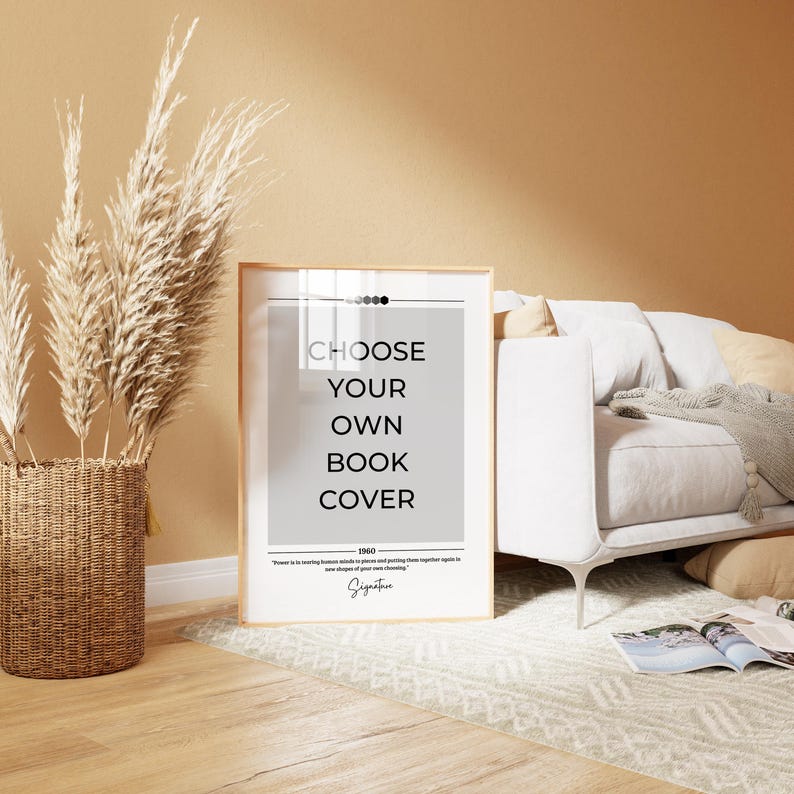 May include: A framed print with the text "Choose Your Own Book Cover" in black text on a gray background. The print is in a wooden frame and is sitting on a white rug in front of a white couch.
