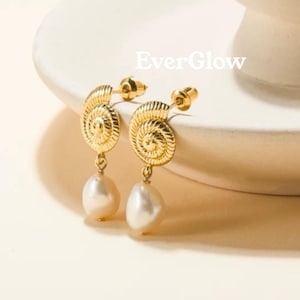 Könnte beinhalten: Ein Paar goldfarbene Ohrringe mit einem strukturierten Spiralmuschel-Design oben und einer hängenden weißen Barockperle unten. Das Wort EverGlow ist in weißer Schrift über den Ohrringen abgedruckt. Die Ohrringe haben einen Steckerverschluss.