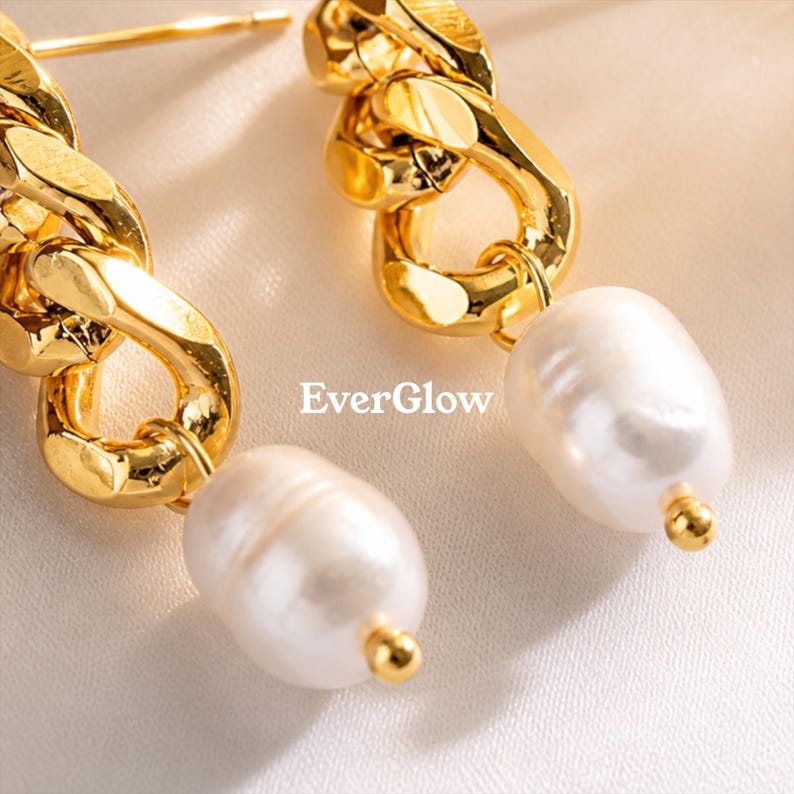 May include: Close-up of gold-colored chain link earrings with white, oval-shaped pearl drops. The earrings have a polished finish and a small gold bead at the base of each pearl. The text "EverGlow" is visible in the image.
