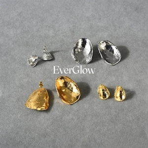Peut inclure: Un ensemble de six boucles d'oreilles en argent et en or. Les boucles d'oreilles sont de formes et de tailles diff&eacute;rentes, et elles ont un aspect textur&eacute; et martel&eacute;. Les boucles d'oreilles sont dispos&eacute;es sur une surface grise. Le texte "EverGlow" est imprim&eacute; en blanc sur la surface.