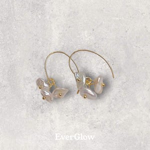 May include: A pair of gold hoop earrings with a cluster of white pearl-like stones dangling from each hoop.