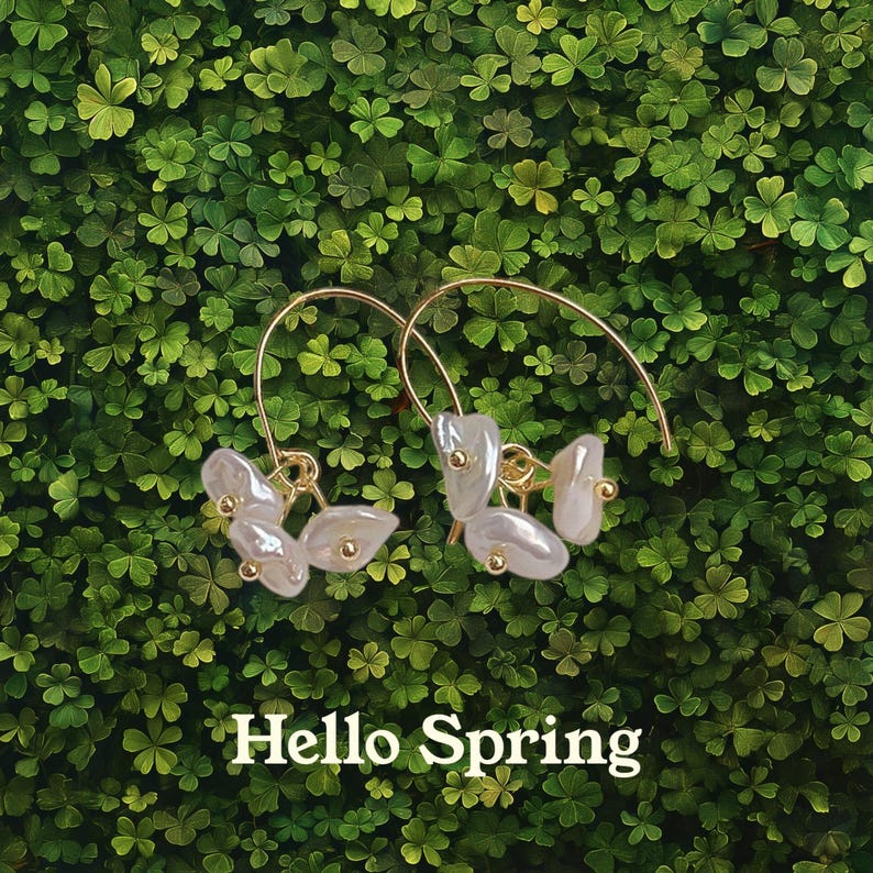 May include: A pair of gold hoop earrings with white pearl-like flower accents. The earrings are on a green background with the text "Hello Spring".