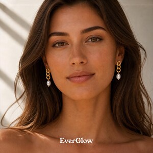 May include: Gold-toned chain link earrings with a single white pearl drop. The earrings are worn by a person with long brown hair. The brand name "EverGlow" is displayed at the bottom of the image.