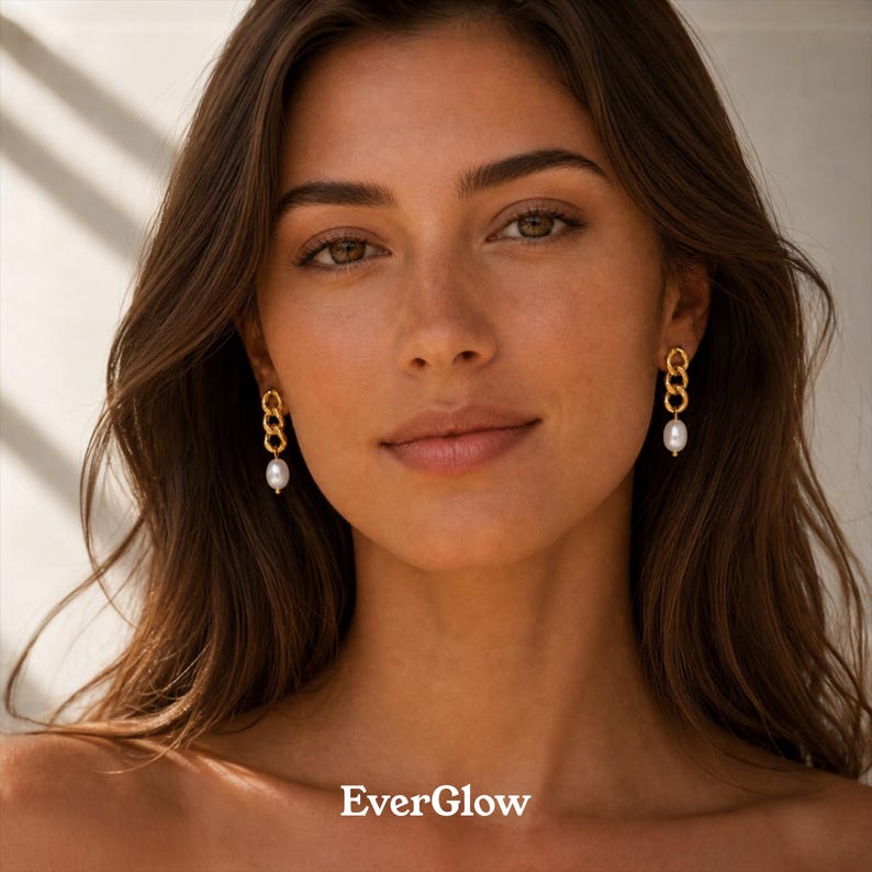 May include: Gold-toned chain link earrings with a single white pearl drop. The earrings are worn by a person with long brown hair. The brand name "EverGlow" is displayed at the bottom of the image.