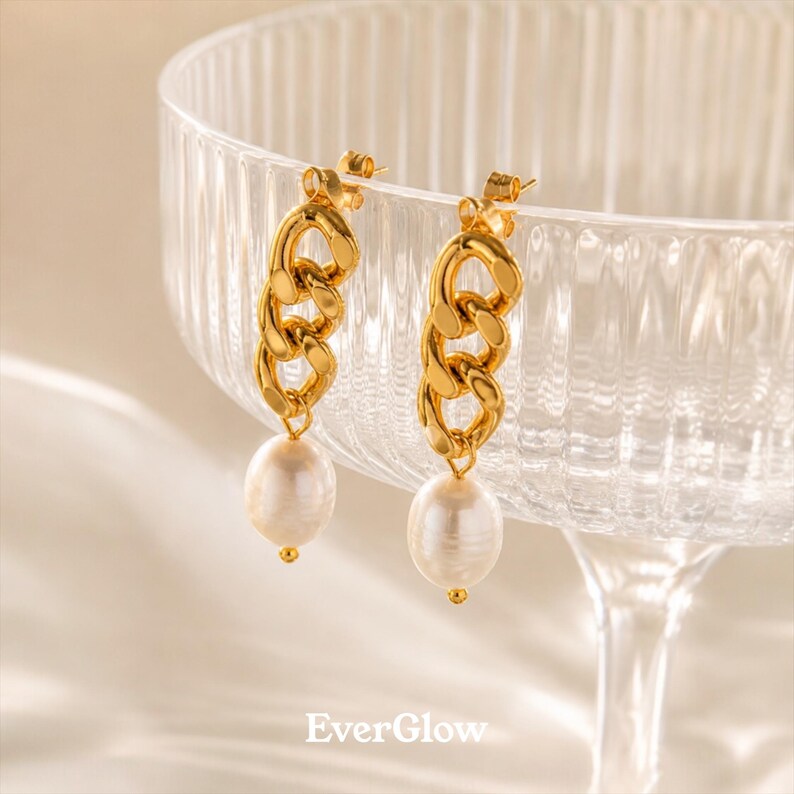 May include: A pair of gold-colored chain link earrings with large, white, teardrop-shaped pearls. The earrings are displayed in front of a clear glass bowl. The brand name "EverGlow" is printed at the bottom of the image.