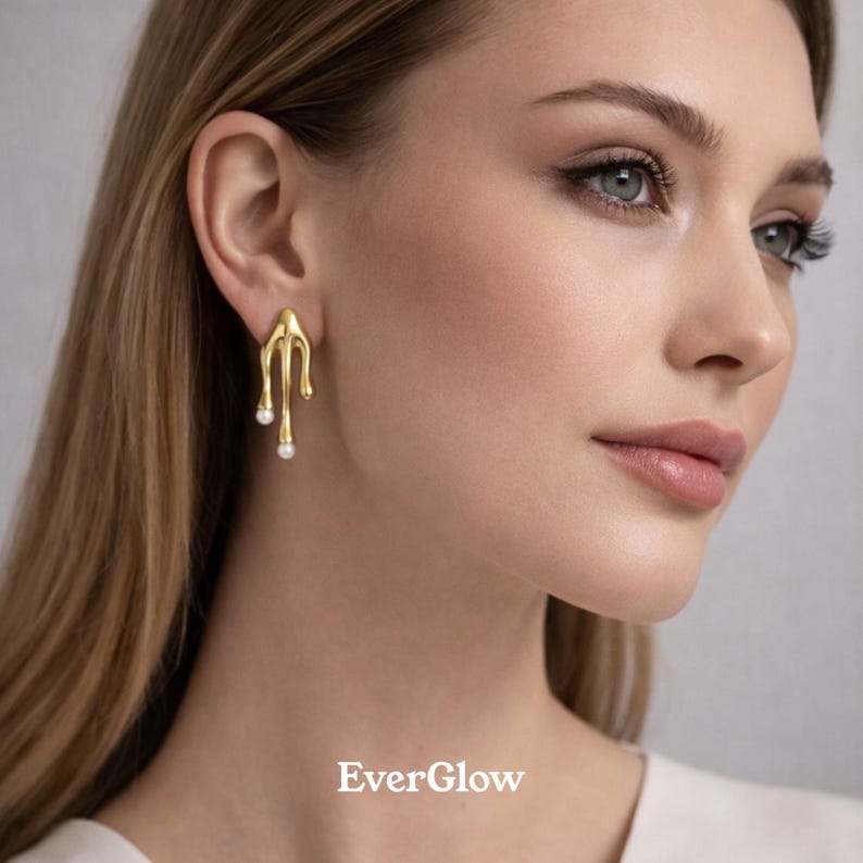 May include: Gold-colored earrings with a unique, dripping design, each featuring a small, dangling pearl. The earrings have a smooth, polished finish and are shown on a person's ear. The brand name "EverGlow" is displayed at the bottom.