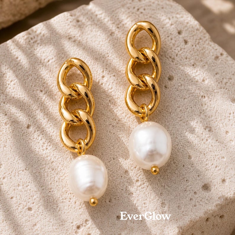 May include: A pair of gold-colored chain link earrings with a large, white pearl drop. The earrings have a polished finish and a small gold bead at the base of the pearl. The brand name "Ever Glow" is visible in the bottom right corner.