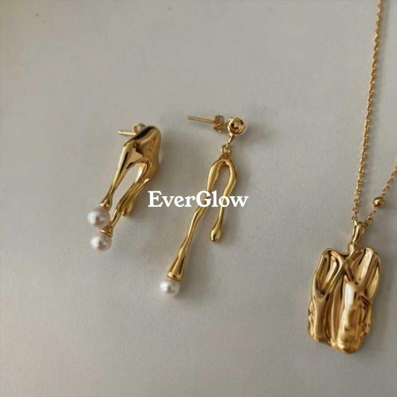 May include: Gold-toned jewelry set featuring a pair of asymmetrical earrings with dangling pearls, and a pendant necklace. The earrings and pendant have a unique, organic design. The text "EverGlow" is visible.