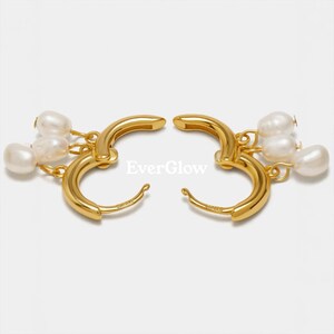 May include: A pair of gold-colored hoop earrings, each adorned with three dangling white pearls. The earrings have a polished finish and a simple, elegant design. The text "EverGlow" is visible.