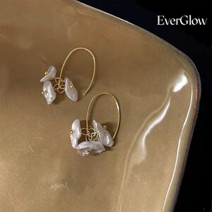 May include: A pair of gold hoop earrings with multiple white pearl-like drops hanging from each hoop. The earrings are displayed on a brown surface with the text "EverGlow" in the top right corner.