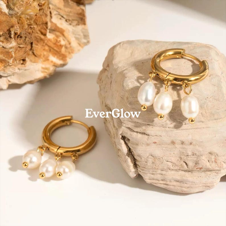 May include: Gold-colored hoop earrings with three dangling white pearls. The earrings are displayed on a light-colored stone surface. The text "EverGlow" is visible in the image.