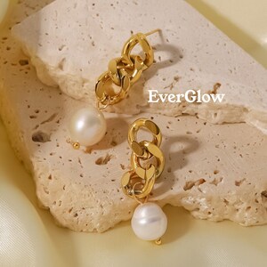 May include: A pair of gold-colored chain link earrings with a pearl drop. The earrings have a post back and are displayed on a textured, light-colored surface. The word "EverGlow" is printed on the surface.