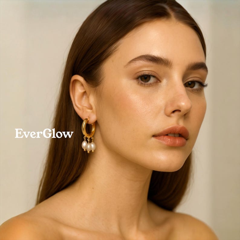 May include: A woman wearing gold hoop earrings with three dangling white pearls. The earrings are a classic design, adding a touch of elegance. The image includes the text "EverGlow" in white letters.