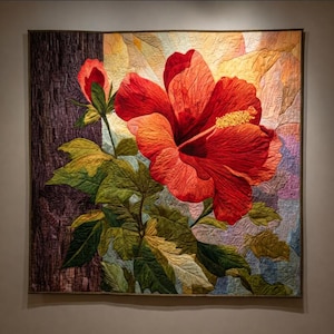 May include: A quilted wall hanging featuring a large, vibrant red hibiscus flower with yellow stamens and green leaves. The background has a textured, multi-colored design. The quilt is framed and ready to hang, showcasing detailed stitching.